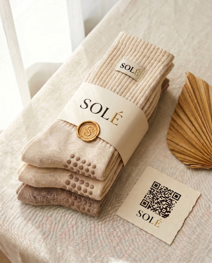 The SOLÉ Grip Socks 3-Pack — three pairs of cream grip socks wrapped in a SOLÉ belly band with a QR care card